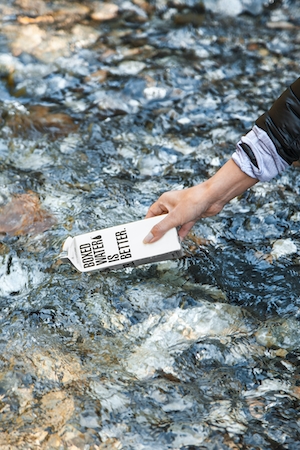 белая коробка с водой в руке человека на фоне мелководья реки 