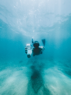 белая коробка с водой в море под водой в руке аквалангиста 