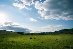 Весенний пейзаж с зеленым полем. Зеленые поля и стога сена на закате, луч света сквозь облака