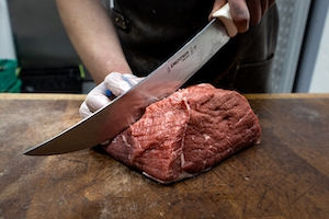 человек режет сырую говядину ножом