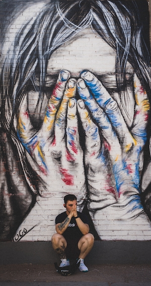 человек сидит на фоне граффити, рисунок женщины, закрывающей руками лицо 
