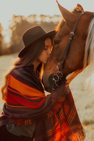 девушка в шляпе целует коричневую лошадь 