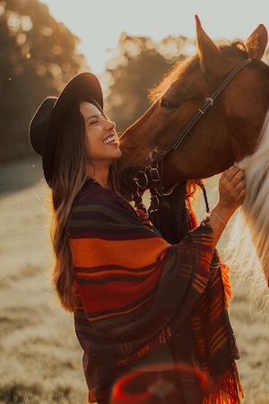 девушка в черной шляпе  и сняраженный коричневый конь, крупный план 