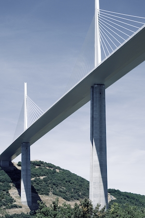 Большой мост на двух опорах на фоне голубого неба и зеленого холма
