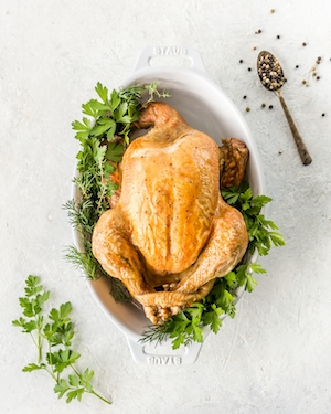 Выращенная на пастбище целая курица, запеченная со свежей зеленью в запеканке из штауба с целыми горошинами перца на белом фоне, крупный план