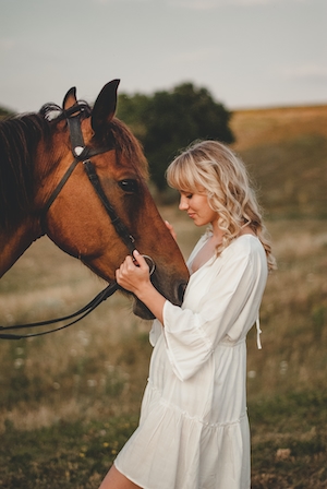 девушка в белом платье и сняраженный коричневый конь, крупный план 