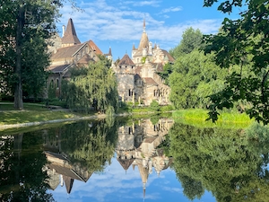 Замок Вайдахуньяд в городском парке, отражение в воде, зеленые деревья и голубое небо 