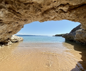 водная гладь, голубое небо, морская бухта с песчаным пляжем и скалистой аркой 