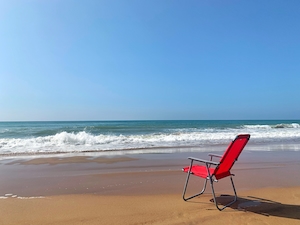 песчаный пляж днем, голубое небо и море, красный стул 