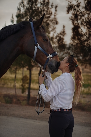 девушка в белой рубашке целует коричневого коня 