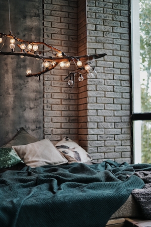 декор комнаты, темно-зеленое покрывало на кровати, люстра в виде ветки, кирпичная стена 