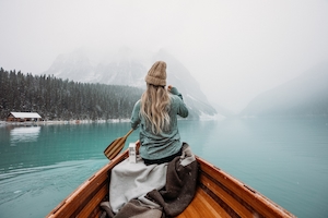 девушка в свитере и шапке плывет на весельной лодке 