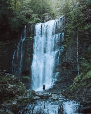 водопад в лесу, поток водопада в лесу, большие скалы, человек на фоне водопада 