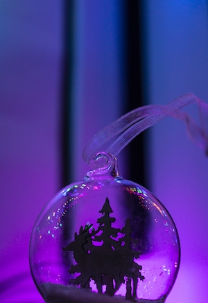 прозрачная елочная игрушка с оленем и елками внутри на фиолетовом фоне 