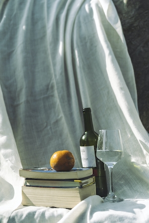книги, бутылка и бокал с вином, апельсин и светлая ткань 