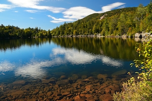 Кристально чистое озеро в горах Адирондак в штате Нью-Йорк. Лес у озера, отражение леса в воде озера, озеро днем