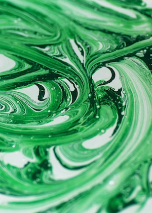 Абстрактные брызги грязно-зеленой краски. Красивые абстрактные узоры, нарисованные зеленой краской на белой поверхности. Вертикальный зеленый гранжевый фон для смартфона и дизайна