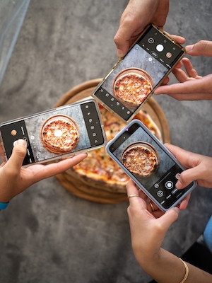 три человека фотографирую пиццу на телефон 