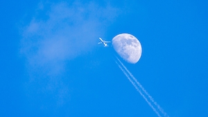 Самолет, летящий высоко на фоне голубого неба с луной 
