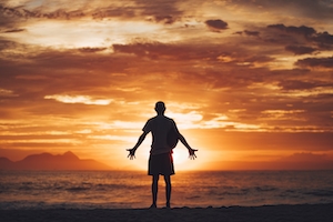 Мужчина, молящийся на пляже во время восхода солнца