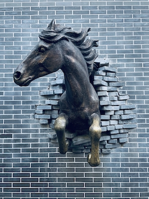 Скульптура коня, выпрыгивающего из кирпичной стены, изготовленная из металла
