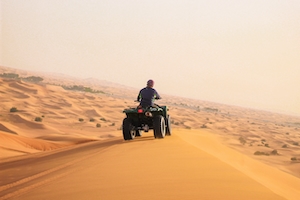 Человек едет на кврадрацикле по пустыне 