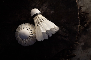 Два белых волана из перьев для бадминтона на темном деревянном фоне.