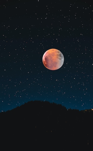 полная луна оранжевого цвета на звездном небе, горы на горизонте 