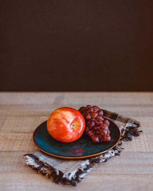 Натюрморт с яблоком и виноградом на тарелке, установленной на тканевой салфетке и деревянной поверхности
