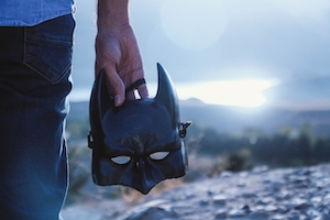 маска Бэтмена в руке человека у озера
