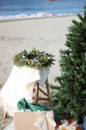Новогодний декор, елка, венок и подарки на пляже на фоне моря 