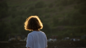 девушка в свете солнца смотрит на зеленый холм, фото со спины 