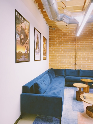 постеры в интерьере на стене в черных рамках, синий диван и кирпичная стена 